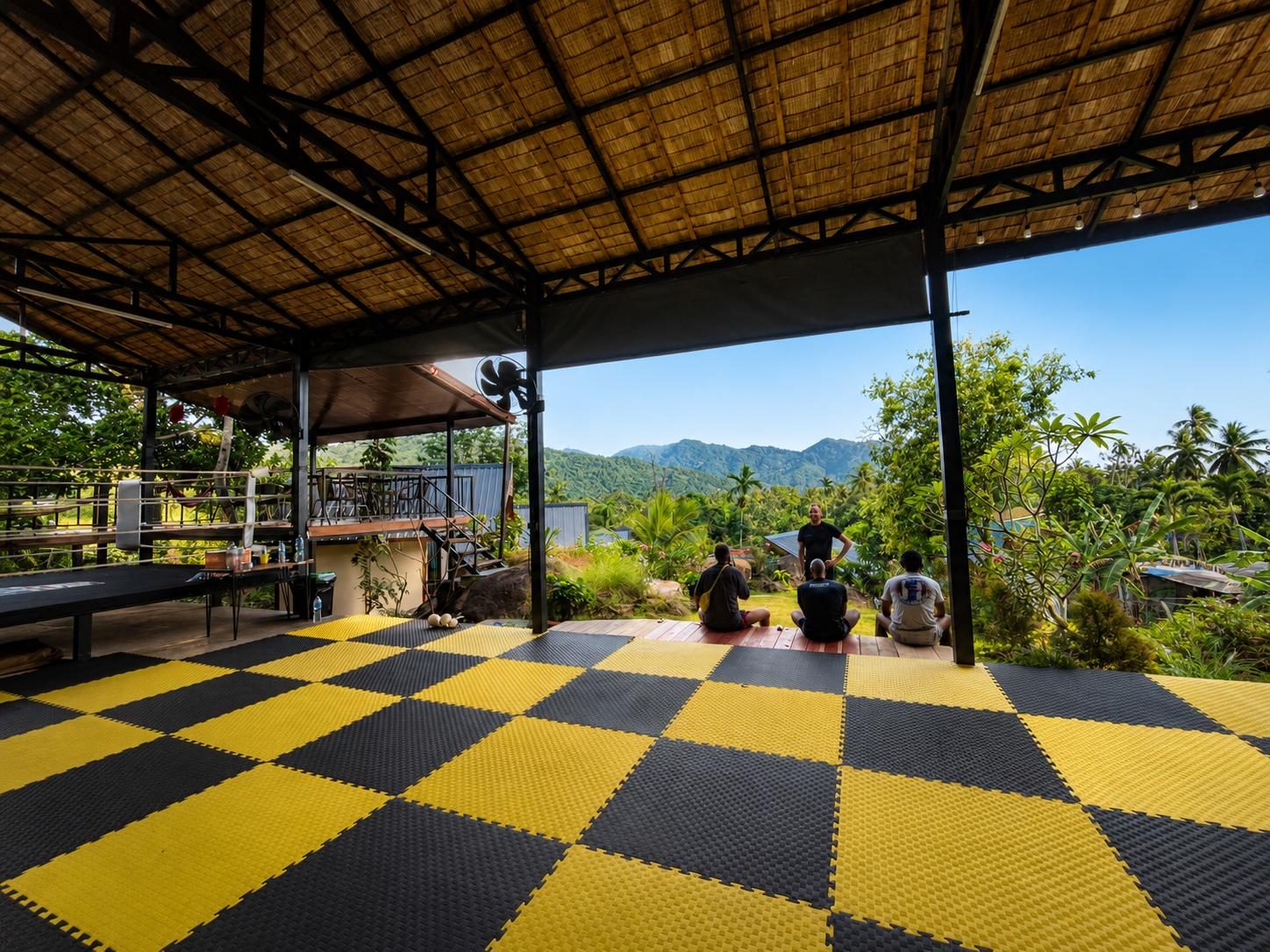 Open-air Muay Thai gym with yellow and black mats, looking out over the green hills of Ban Tai